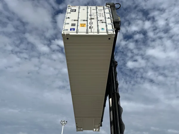 Low-angle crane lift of an OWLU 95002 reefer container against sky background